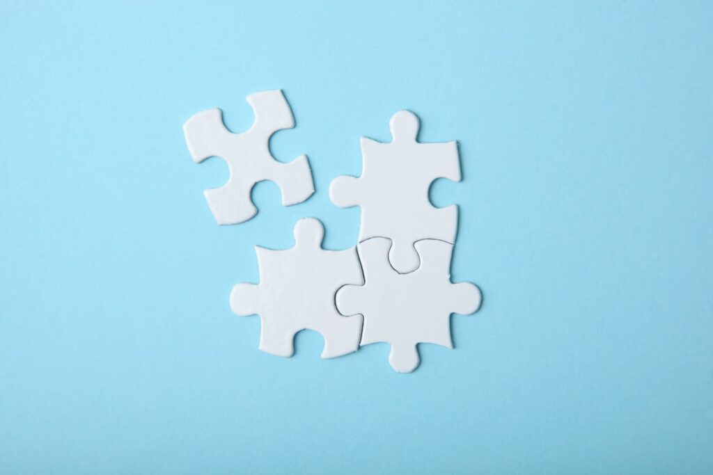 Das Bild zeigt vier weiße Puzzleteile auf hellblauem Untergrund. Drei Puzzleteile sind bereits verbunden, das vierte wird gerade eingesetzt. Es symbolisiert die vier kognitiven Prozesse, die bei der Beantwortung einer Frage in einem Fragebogen ablaufen. Wer komplexe Themen erfassen und abfragen will, muss diese kennen und berücksichtigen.